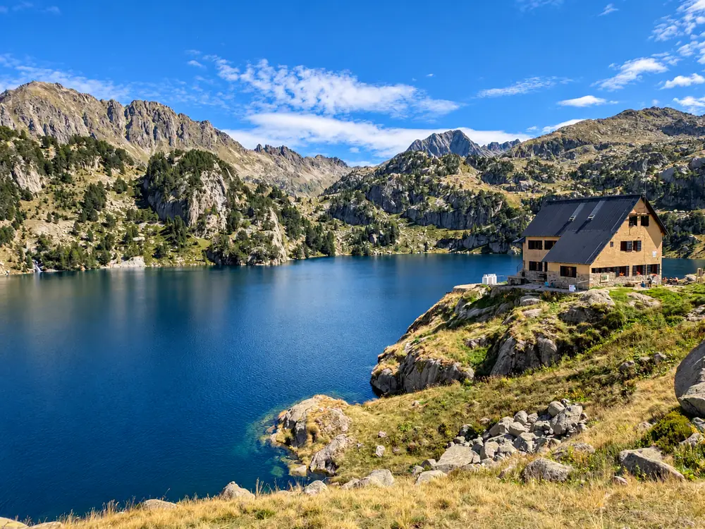 Refugio de montaña junto a un lago de alta montaña rodeado de picos, en el Pirineo catalán